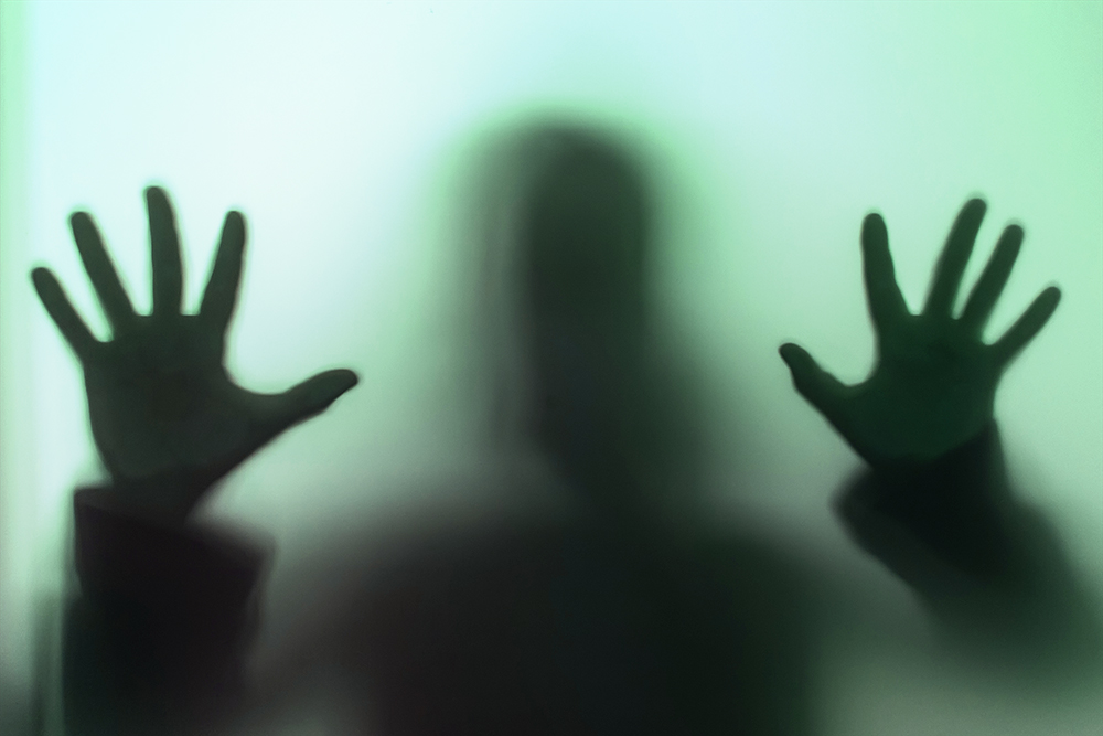 A blurry silhouette of a human figure behind frosted green glass. 