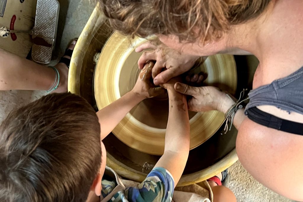Two people creating a pot from clay. One is assisting the other.