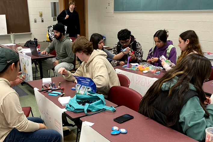 A group of people sitting at numerous tables doing crafts.