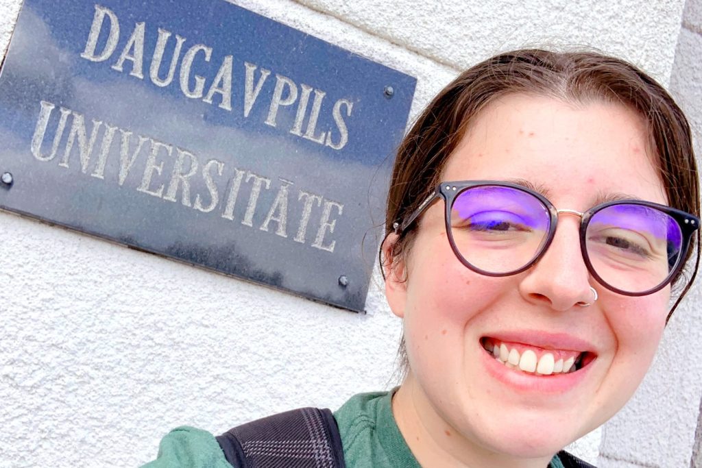 Selfie of someone smiling in front of a sign that says “Daugavpils Universitāte.”