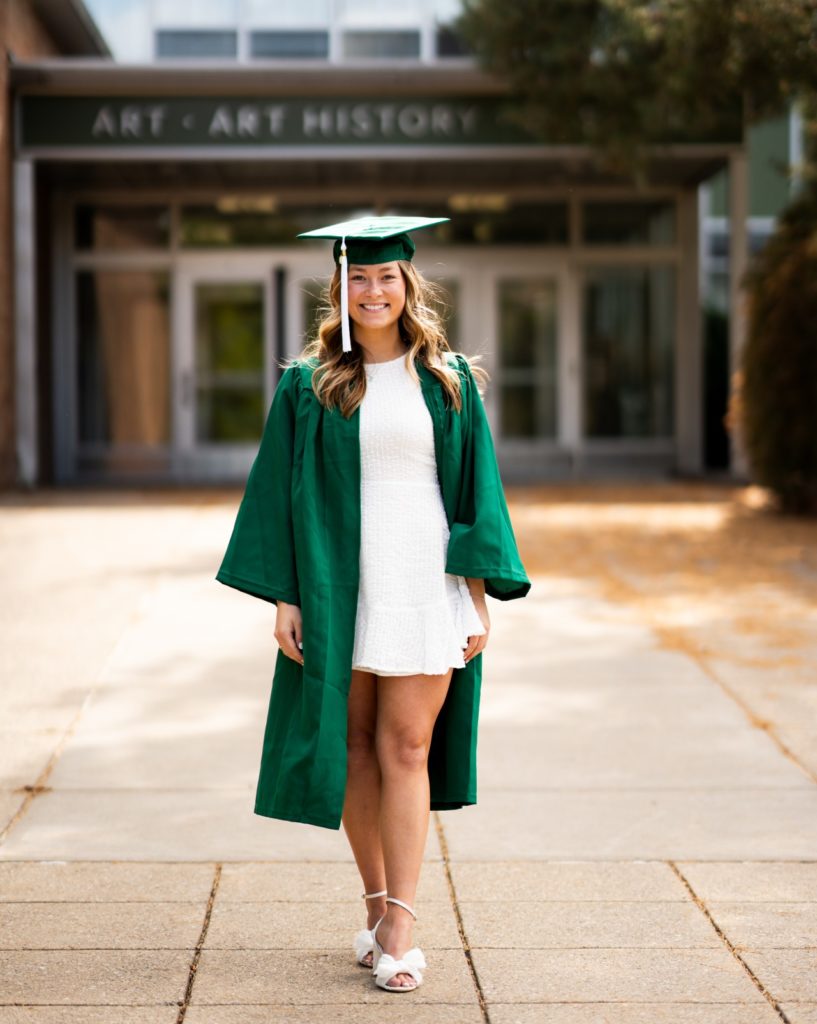 Woman in a green graduation cap and gown with a white dress.