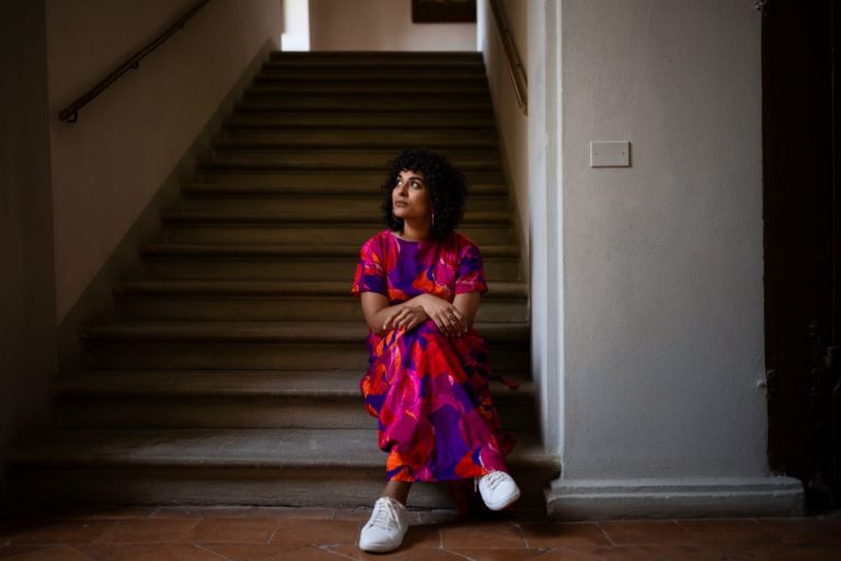 a woman in a colorful dress sits at the bottom of a flight of stairs. Photo taken by Marco Giugliarelli.