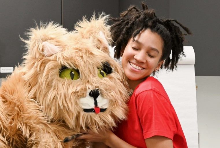 Person in a light brown cat costume being hugged by a woman in a red shirt.