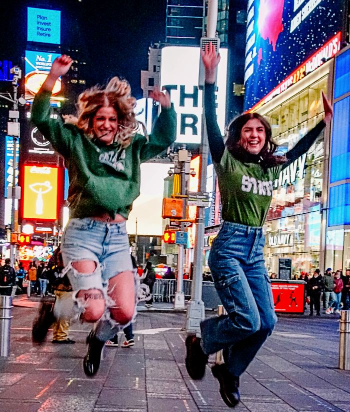 Two women jumping up in the air in the middle of Times Square. 