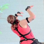 Photo of woman in a strange position with technology strapped to her joints. In front of her a green animated character in following her same movement.