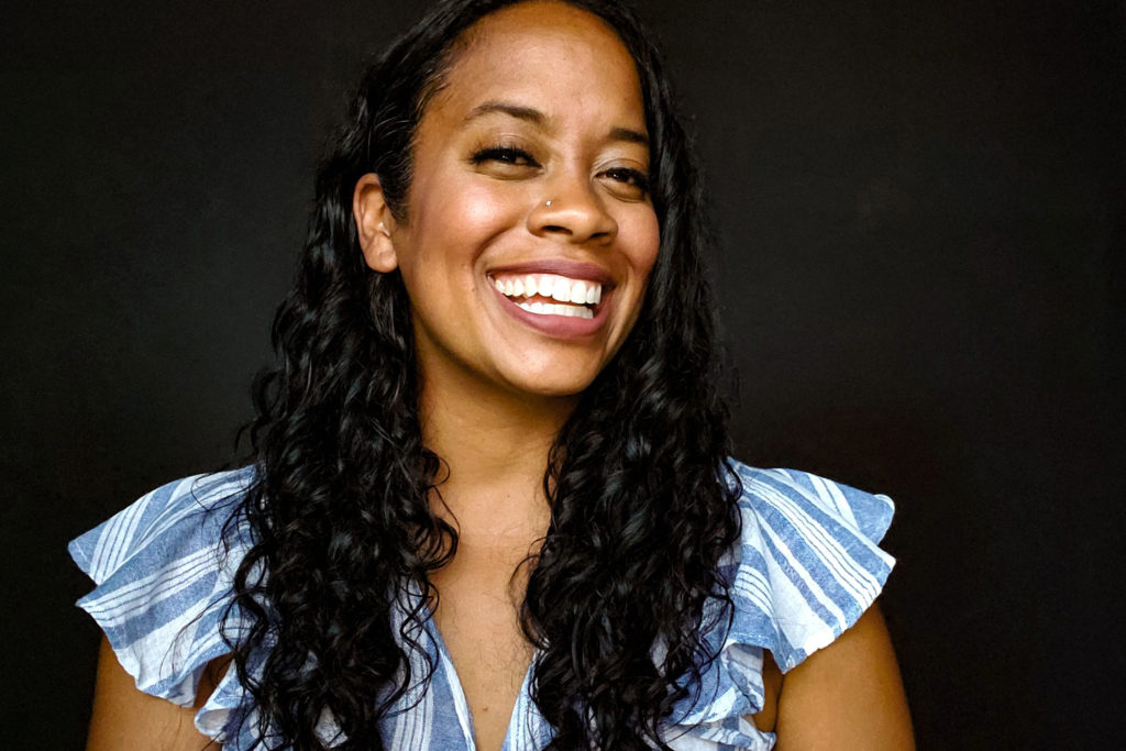 A picture of a woman smiling. She has long black hair and wears a blue and white shirt. 