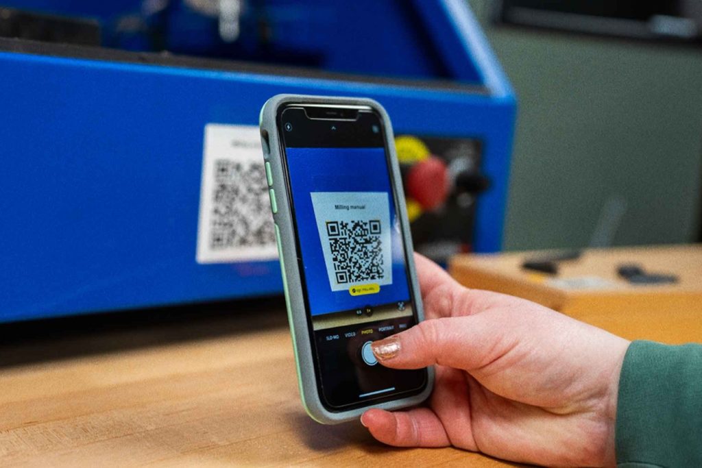 Photo of a hand scanning a QR code with a phone indoors.