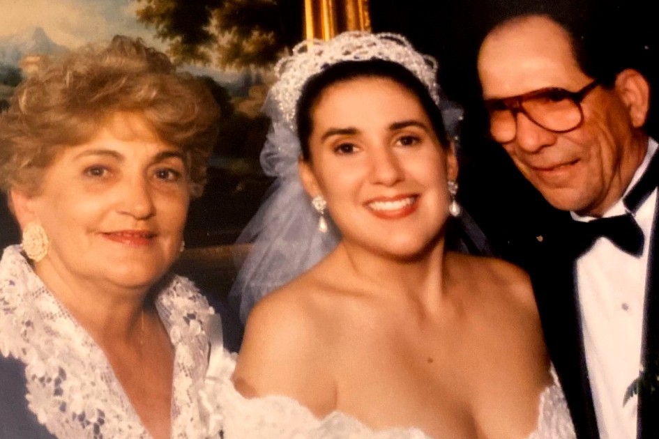 A pitcure of three people. On the left is a woman with short blonde hair. In the middle is a woman in a white wedding gown. On the right is a man in a tuxedo. 