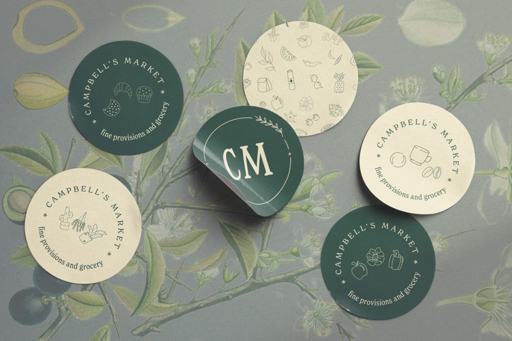 six round green and white stickers that say Campbell's Market on them, laying on a printed green background. 