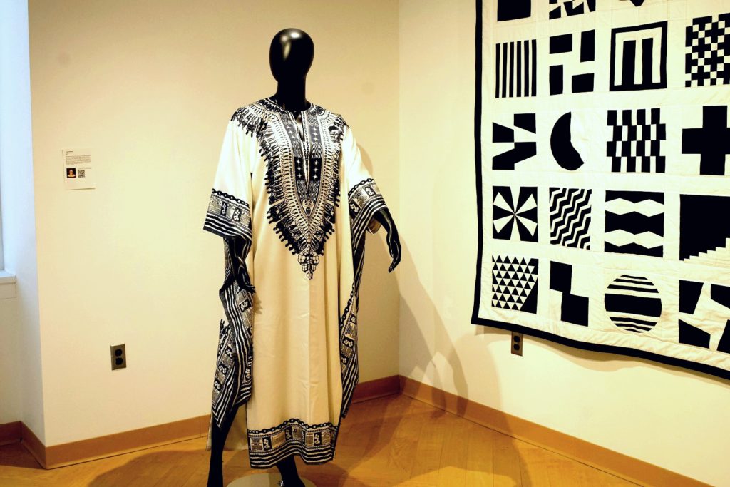 The Afrofuturism & Quilts Exhibit showing a black and white quilt hanging on a wall with a mannequin standing next to it wearing a black and white dress. 