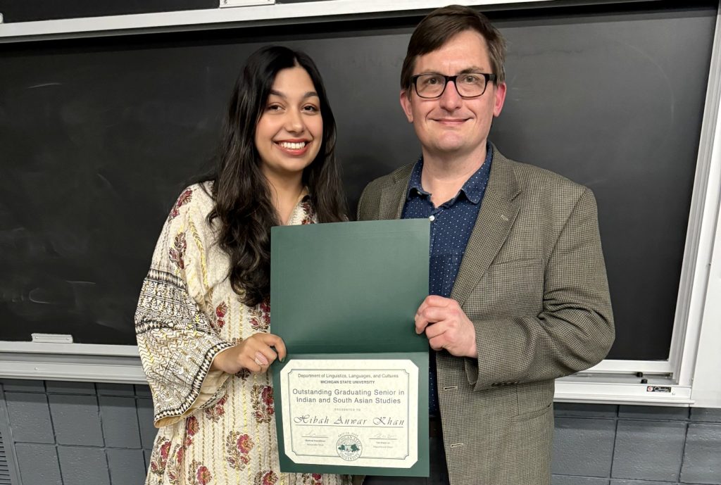 A picture of two people standing in front of a blackboard holding an award.