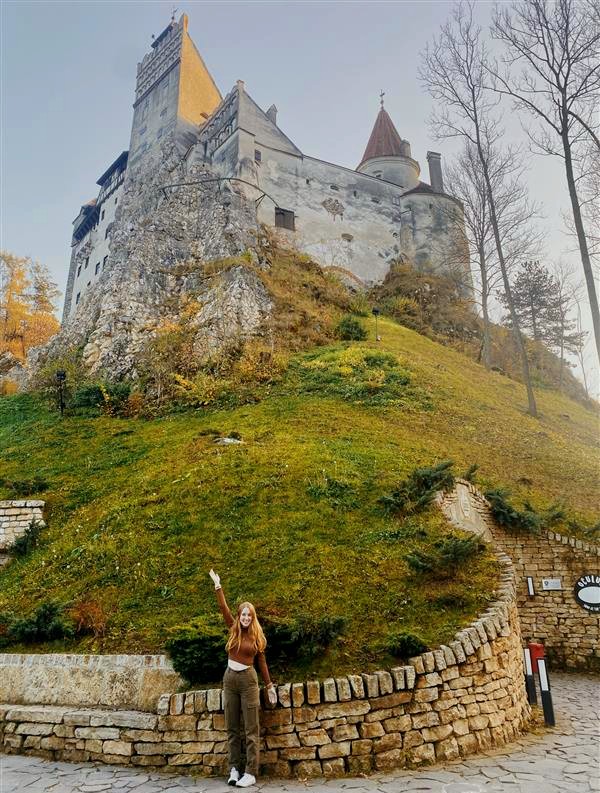 A woman sanding with outstretched arms and a castle behind her. 