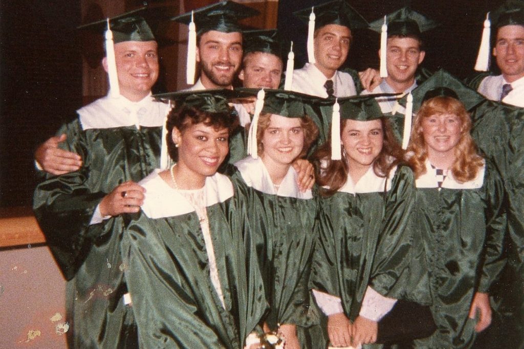 A faded photo of a group of people in green and white graduation gowns.