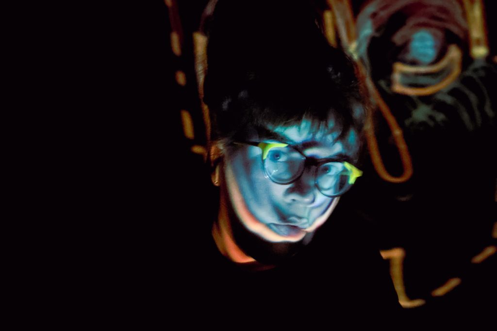 A artistic photograph of a person in a dark room with glasses, illuminated by a blue light. 