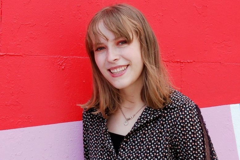 A picture of a woman in a dotted shirt in front of a colorful wall.