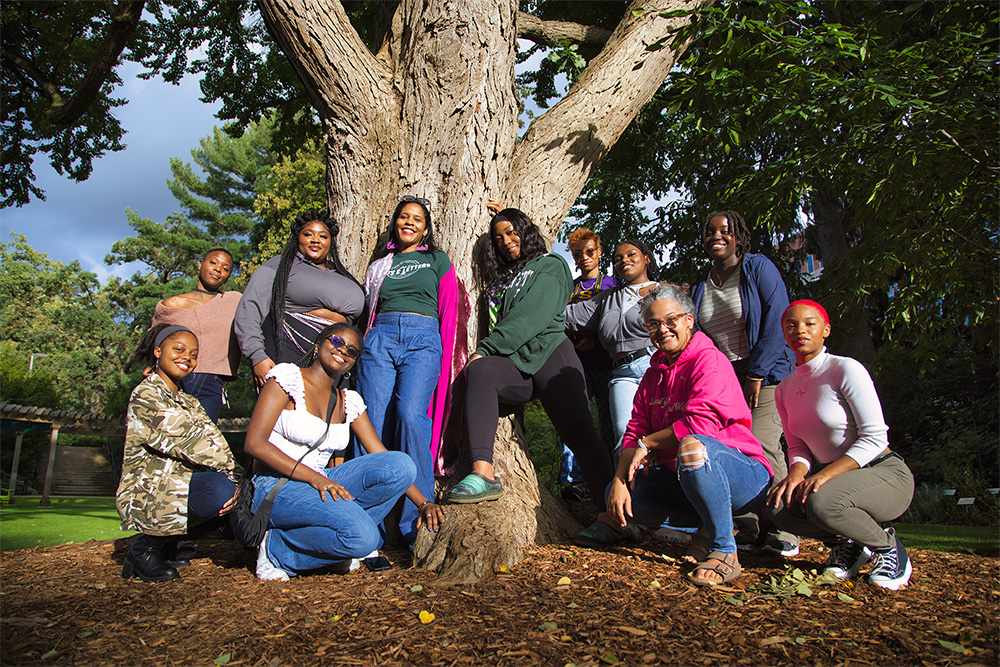 A group of students and faculty pose together next to a large tree in the W.J. Beal Botanical Garden on the campus of Michigan State University.
