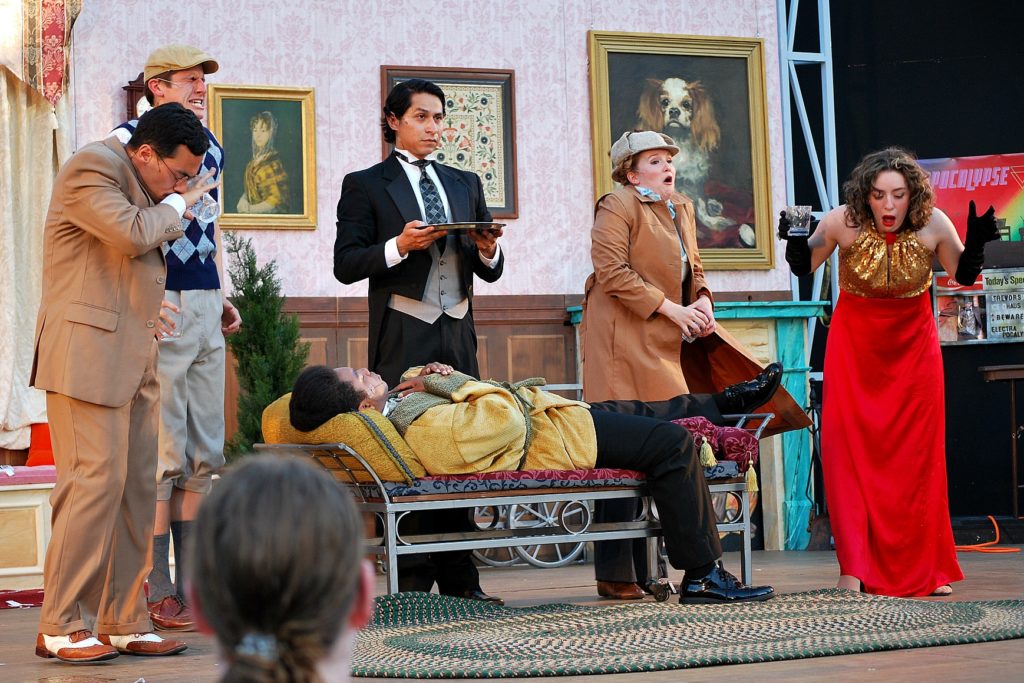 five actors on stage performing the play, "Clue" on an outdoor stage. 