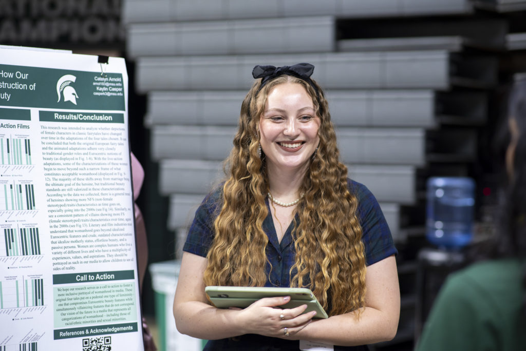 Woman with long hair standing next to a research poster. 
