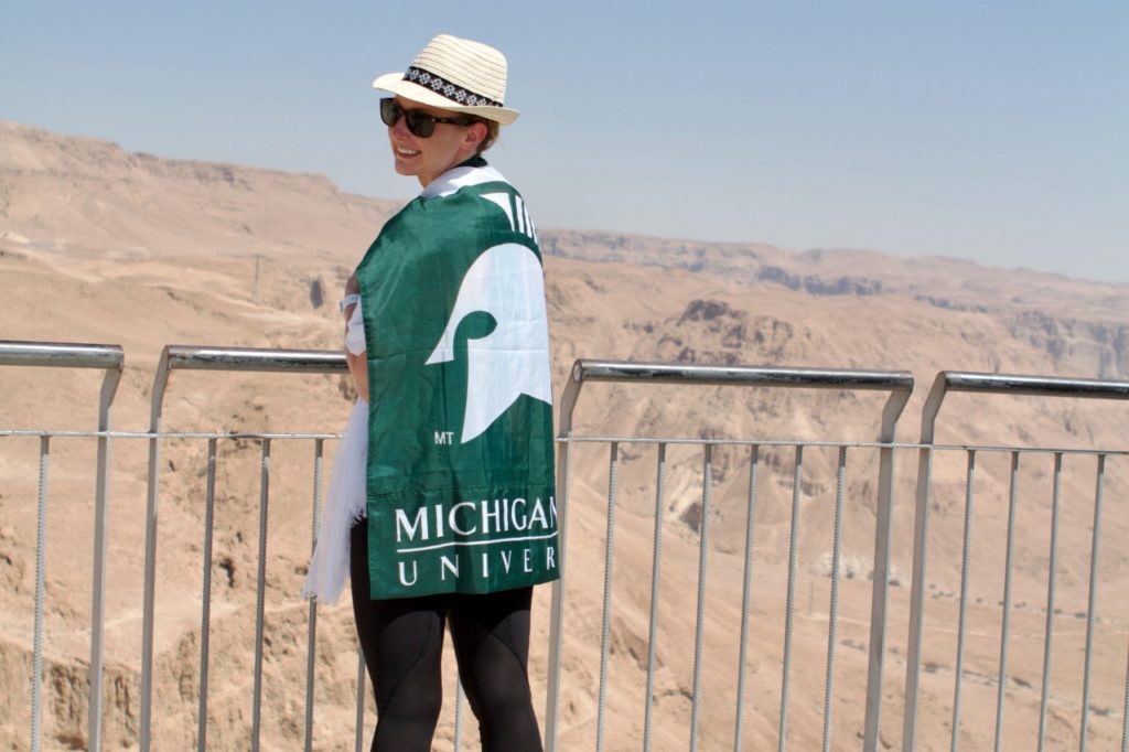 Photo of Lauyren Haight on one of her study abroad trips standing at a scenic desert overlook wrapped in a Michigan State University flag.
