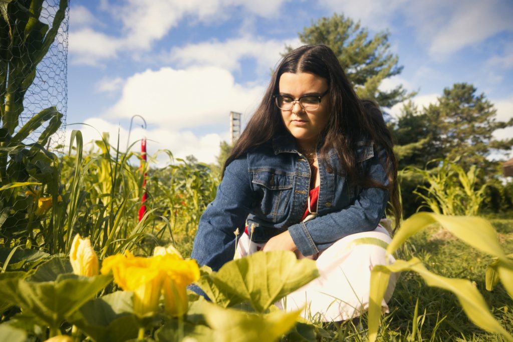 A picture of a person in a jean jacket and a white and red dress kneeling in a green garden