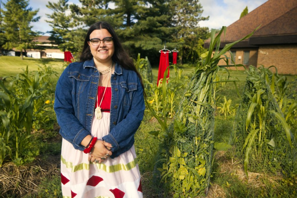 A picture of a person in a jean jacket and a white and red dress standing in a green garden