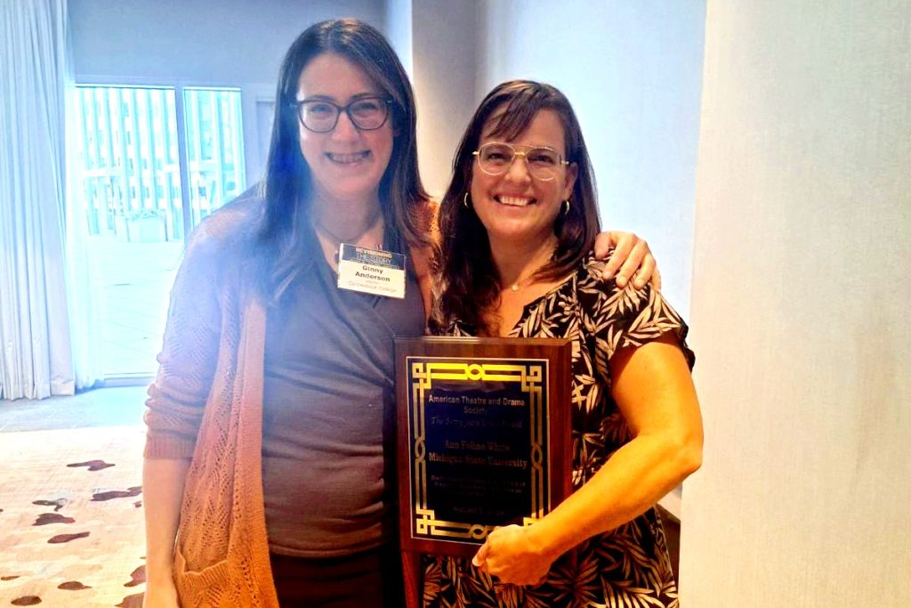 Two women standing next to each other with teh one of the left holding a plaque. 