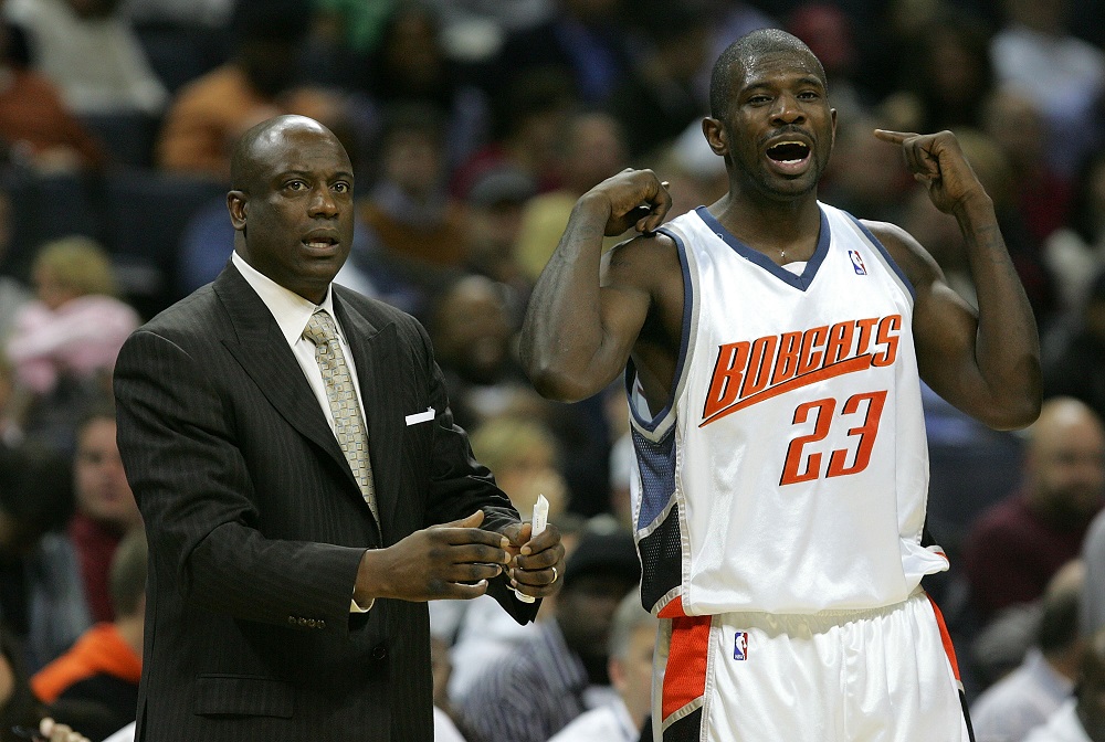 A coach in a suit gestures while standing next to an basketball player wearing a Charlotte Bobcats jersey during a game.