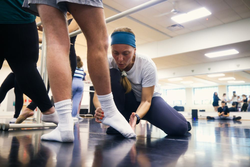 A dance instructor helps students point their toes in the proper dance position.