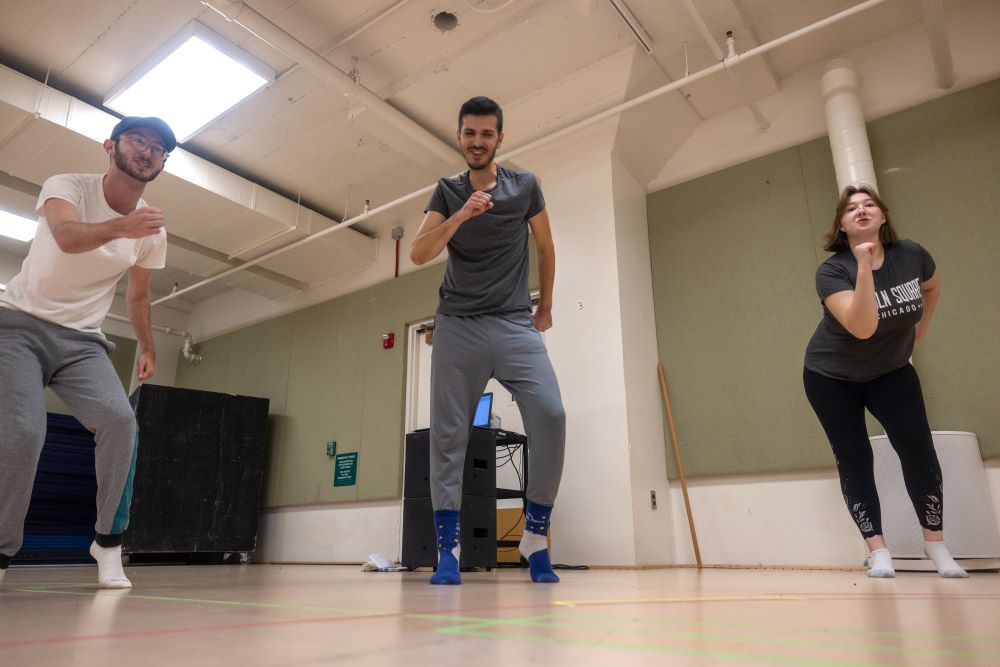 Two students mirror the movement instructor in between them as they perform exaggerated walking-in-place movements.