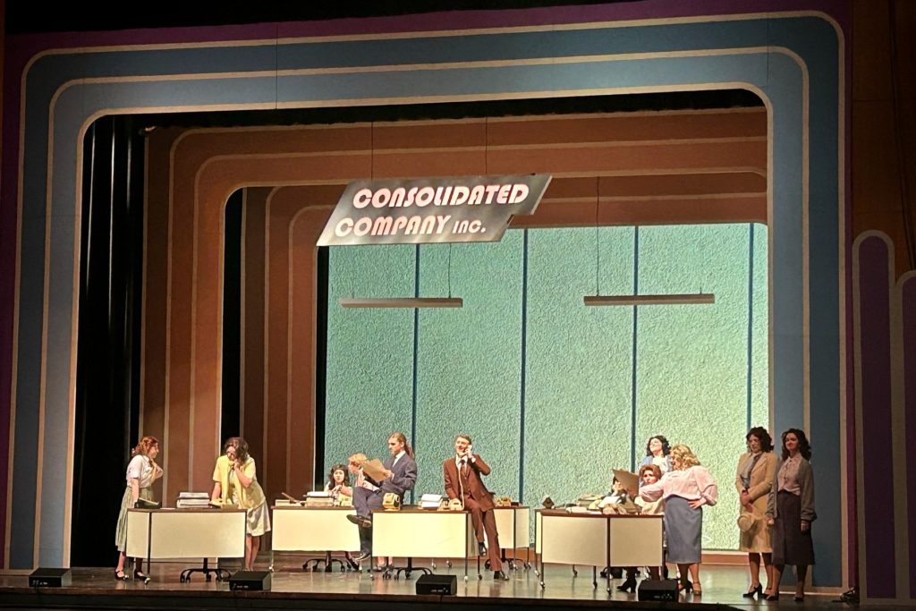 An office setting with 10 different people that is up on stage for the "9 to 5: The Musical" setting.