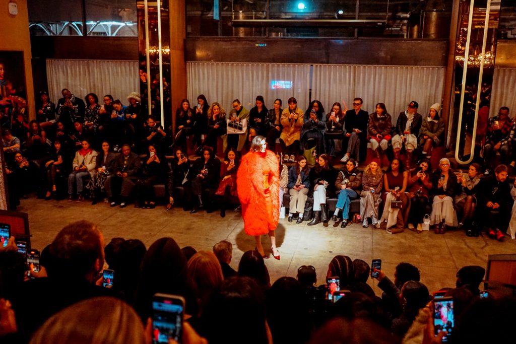 A fashion show audience watches as a model walks down the runway in a striking red. 