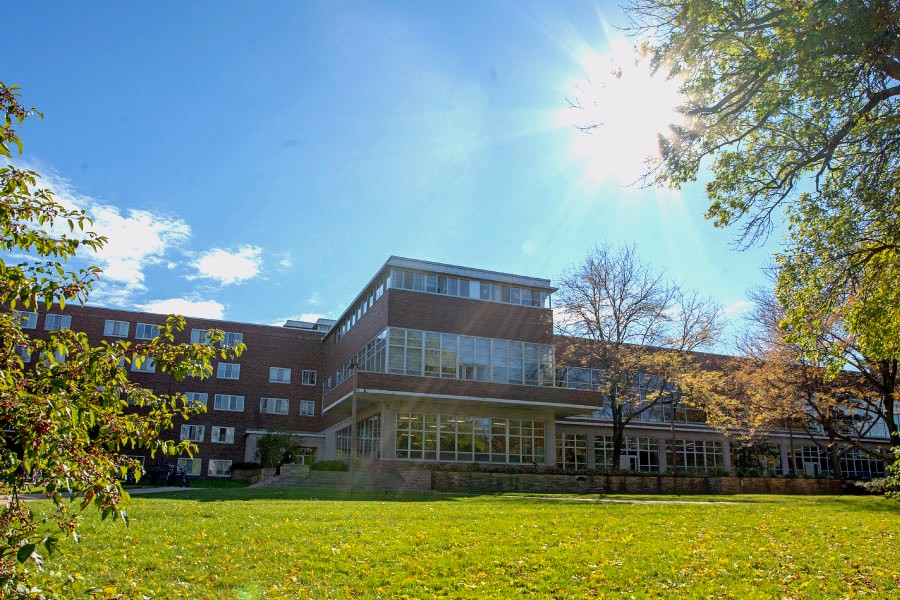 A large brick residence hall on a sunny day, surrounded by green trees and a bright lawn. 