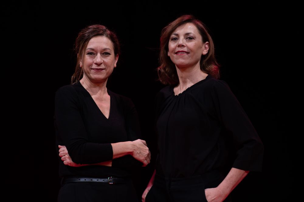 Two women dressed in black stand side by side and smile. Photo by Federico Sigillo.