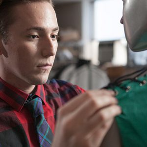 a person with a plaid shirt and colorful tie working on a dress on a mannequin